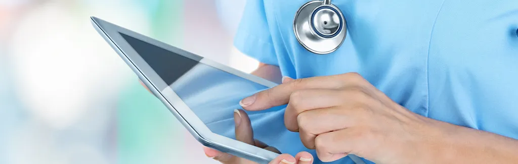 A nurse in blue uniform tapping on a tablet.